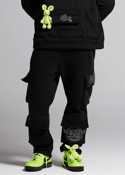 Person wearing black cargo pants with green accents and neon green shoes on a gray background