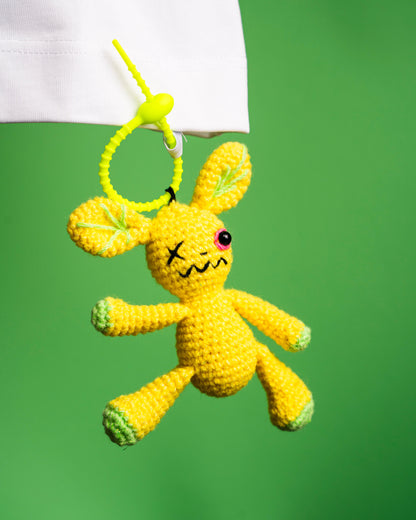 Yellow crocheted bunny toy with a sad face on a green background