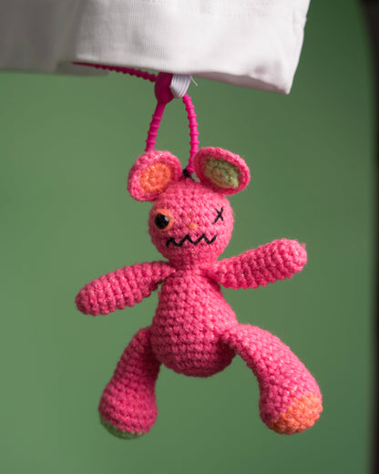 Pink crocheted creature with a sad face hanging from a string against a green background