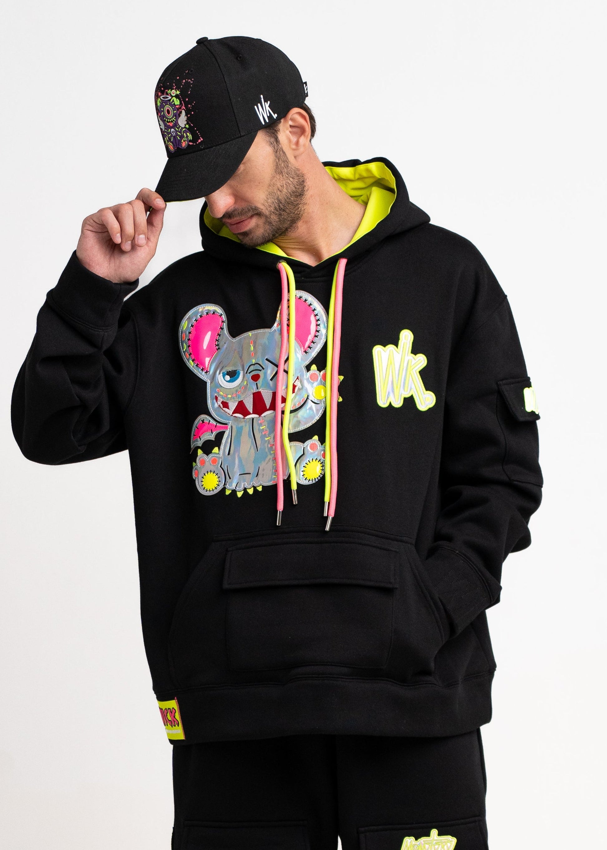 Person wearing a black hoodie with colorful graphics and black pants on a white background
