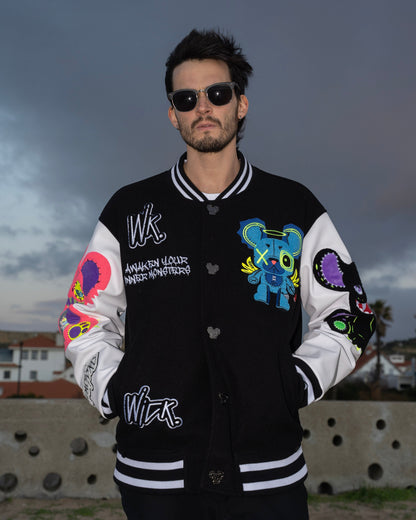 Man wearing a black and white varsity jacket with colorful designs and text, standing against a cloudy sky.