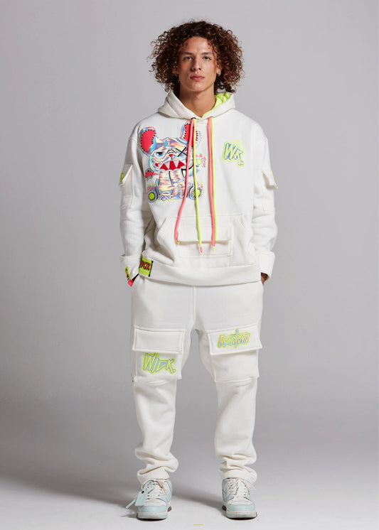 Person wearing a white hoodie and pants with colorful designs on a gray background
