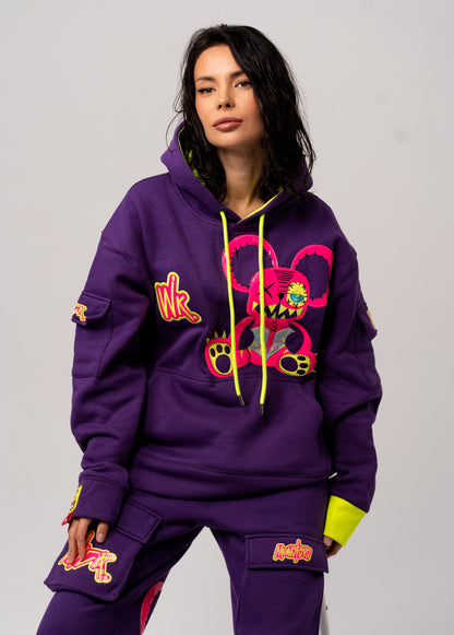 Person wearing a purple hoodie and pants with colorful designs on a plain background