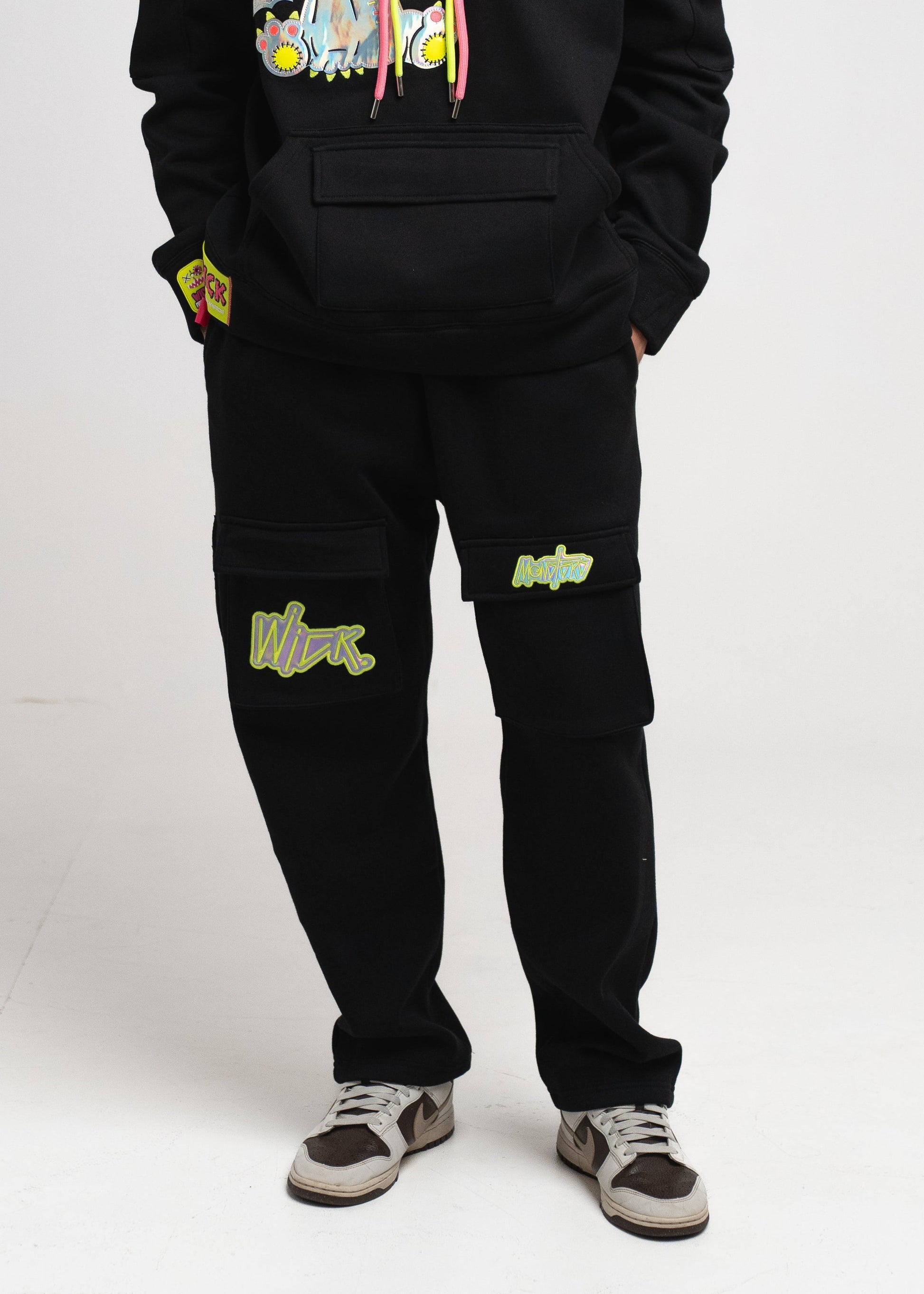 Person wearing a black hoodie with colorful graphics and matching pants on a white background