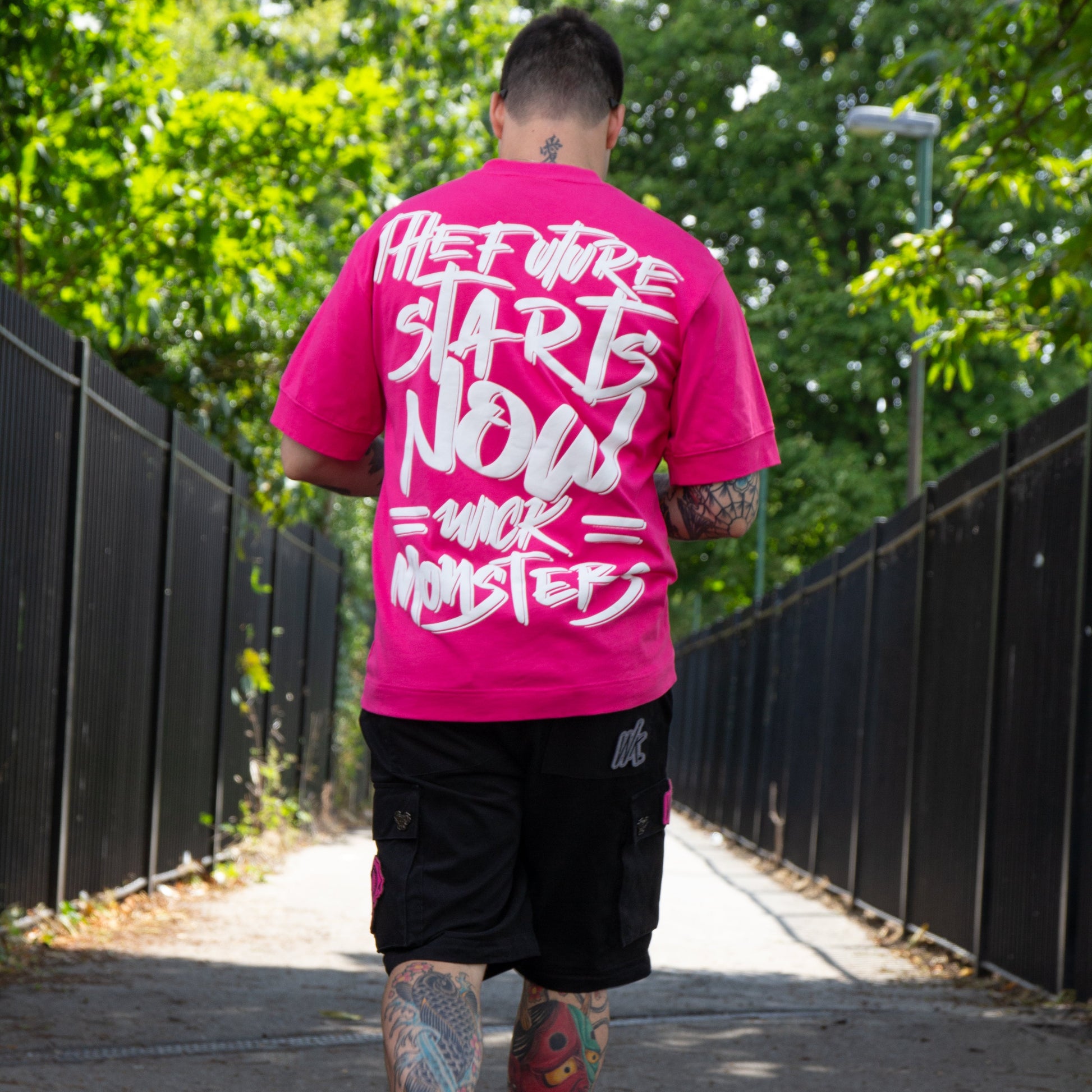 Person wearing a bright pink t-shirt with text, walking on a path with greenery.