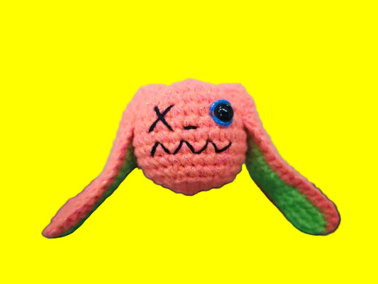 Pink crochet creature with a sad face on a green cutting mat