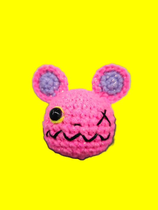 Pink crochet mouse toy with purple ears on a green cutting mat